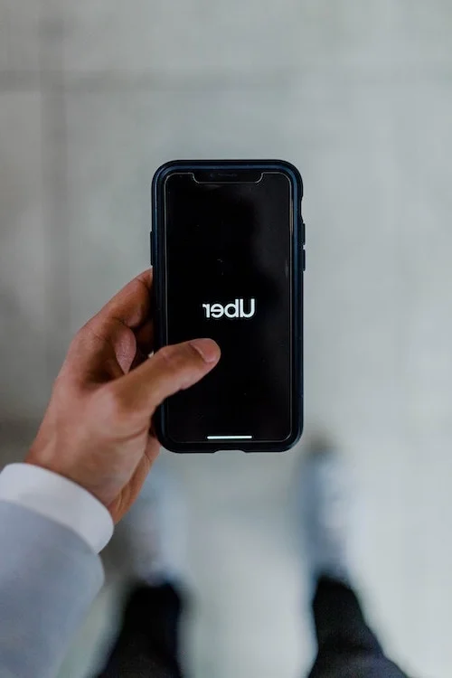 Man holding up a mobile phone with Uber logo displayed on the screen.