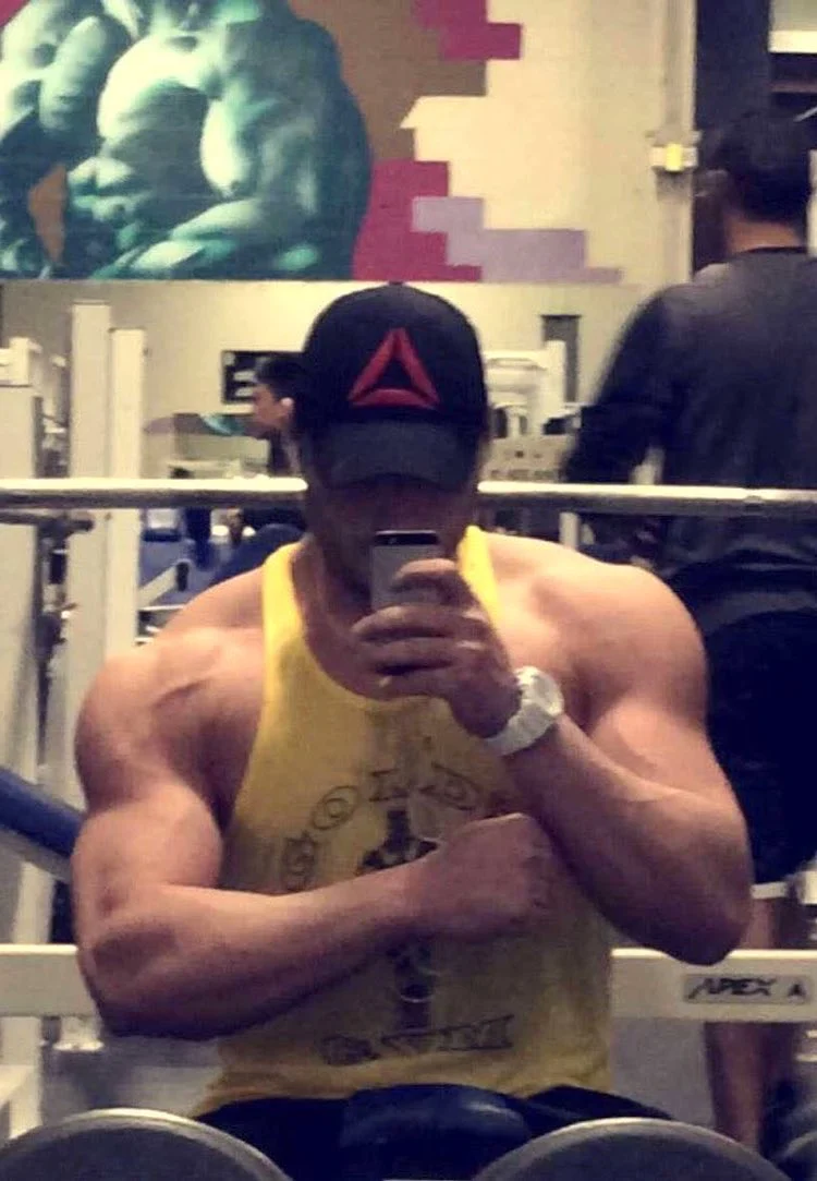 Image of Jon Zherka flexing his muscles in a gym in front of a mirror