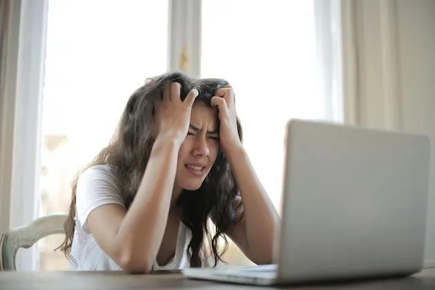 Femme irritée assise devant un ordinateur, semblant frustrée.