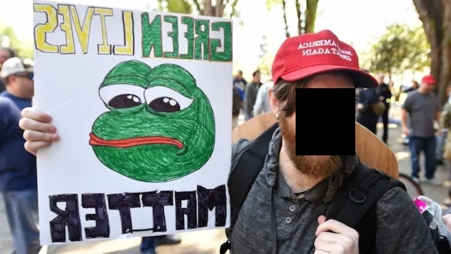 A man at a political rally holding a sign that reads 'Green Lives Matter', while wearing a 'Make America Great Again' hat, embodying the contradictory and performative nature of a 'wignat', a term used to describe individuals who adopt extreme nationalist views in an exaggerated and attention-seeking manner.